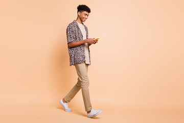 Fototapeta na wymiar Full size profile photo of brunet optimistic guy going look telephone wear modern shirt trousers sneakers isolated on beige background