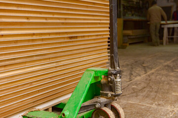 Manual forklift loaded with wooden, glued profiles in warehouse of carpentry