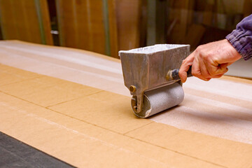 Carpenter smears the plywood with hand roller tool, spreader for evenly application of glue on the wooden surface