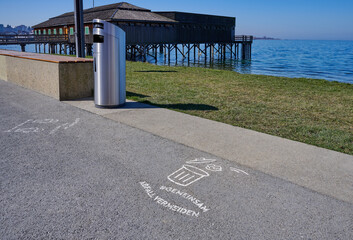 Mülleimer auf dem See Ufer promenade und die Inschrift auf dem Asphalt mit dem Slogan, Abfall in den Mülleimer zu werfen und müllentsorgen