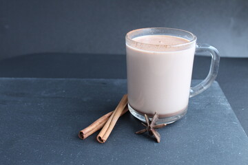 cocoa hot chocolate in a glass mug with cinnamon sticks and badyan on a black background with a place to text a copyspace