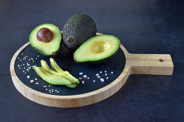 Overthrowing green avocados cut on a dark cutting board with spices