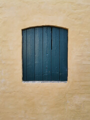 old green closed window with shutters in a yellow wall