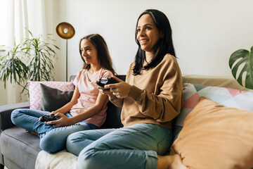 Single parenthood. Mother and daughter playing video games together at home.