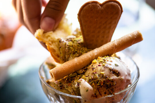 Hand scooping pistachio ice cream with brioche in a cup with garnishments