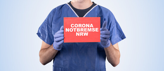 Arzt hält Schild mit Aufschrift Corona Notbremse NRW
