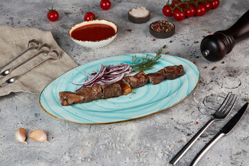 Shish kebab with red onion and sauce on a plate
