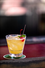 Yellow alcohol cocktail with red cherry served in bar counter