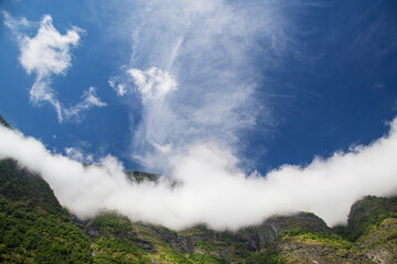 Fototapeta na wymiar Clouds lie on the tops of the mountains in clear weather. Panoramic view