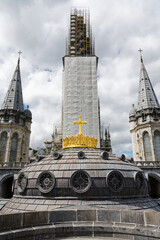 Fototapeta premium Lourdes, France - 22nd august 2020 : Detail of the golden cross on the dome of the basilica of the holy city of Lourdes in front of the work on the main bell tower. Central symmetry