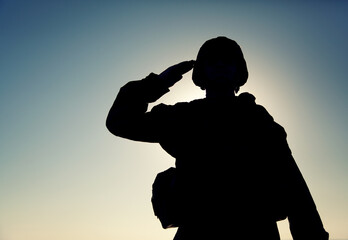 Silhouette of soldier in combat helmet and ammunition saluting on background of sunset sky. Army...