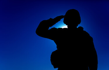 Silhouette of soldier in combat helmet and ammunition saluting on background of sunset sky. Army special forces fighter, Marines rifleman showing respect, greeting officer with salute gesture