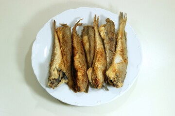Fresh fried codling young fishes in olive oil on a white plate. Top view
