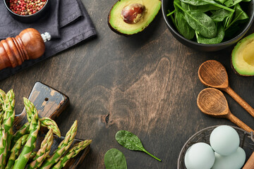 Fototapeta na wymiar Bunch of fresh green organic asparagus spinach, avocado, chicken eggs and pepper seasoning on black old wooden background, top view. Food cooking background with copy space. Mock up.