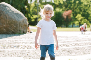 Cute cheerful girl playing in fountain. Kid in white shirt having fun in summer park