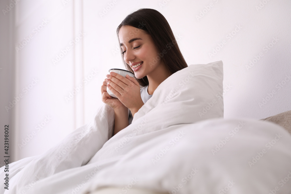 Poster Woman covered in blanket holding cup of drink at home