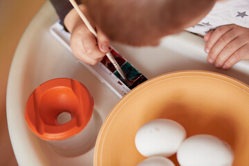 Easter preparation: Toddler paints easter eggs. Happy Easter concept. Child is developing fine motor skills with bright paints.
