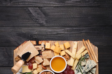 Cheese plate with honey, grapes and nuts on black wooden table, top view. Space for text