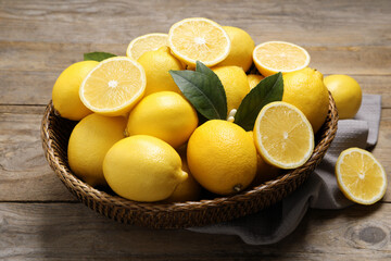 Many fresh ripe lemons with green leaves on wooden table