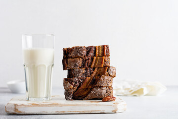 Banana bread cut into slices in stack with glass of milk on plain gray concrete background. Selective focus