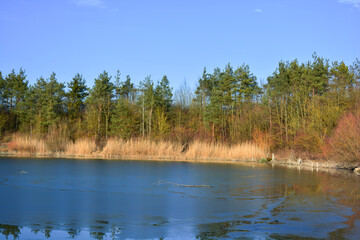 Eis auf dem Gipssee bei Donnersdorf mit Bäumen und blauem Himmel, in der Nähe vom Zabelstein in Franken, Bayern, Deutschland