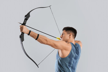 Man with bow and arrow practicing archery on light grey background