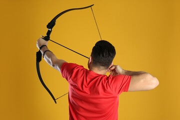 Man with bow and arrow practicing archery on yellow background, back view