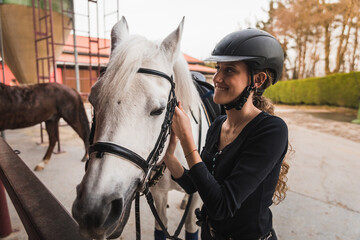 Young caucasian woman preparing a white horse for a ride