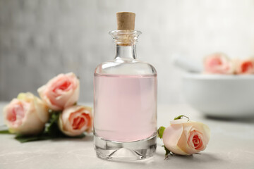 Bottle of rose essential oil and flowers on white table