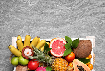 Different tropical fruits in wooden box on grey background, top view. Space for text