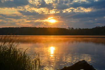 Sonnenaufgang über einen See mit Spiegelung im Wasser und Nebelschleier am frühen Morgen...