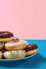Life is sweet. Cropped shot of various colourful round glazed donuts with sprinkles on the plate over blue and pink background