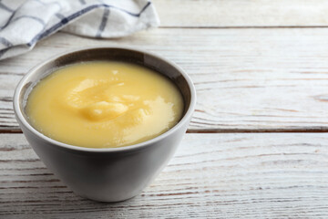 Bowl of Ghee butter on white wooden table, closeup. Space for text