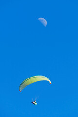 Paraglider and half moon against light blue sky