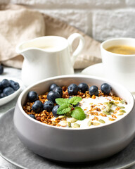 Homemade organic buckwheat granola with yogurt, blueberries, hazelnuts, peanuts, nutmeg, pumpkin seeds and flax seeds in a ceramic bowl on a light background. Breakfast for healthy 