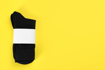 Fototapeta na wymiar Pair of black cotton socks on yellow background, top view. Space for text