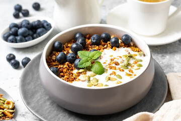 Homemade organic buckwheat granola with yogurt, blueberries, hazelnuts, peanuts, nutmeg, pumpkin seeds and flax seeds in a ceramic bowl on a light background. Breakfast for healthy 