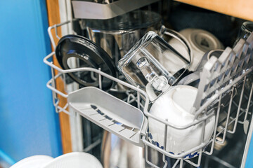 Clean dishes in the open dishwasher in the kitchen with light blue facades