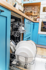 Clean dishes in the open dishwasher in the kitchen with light blue facades