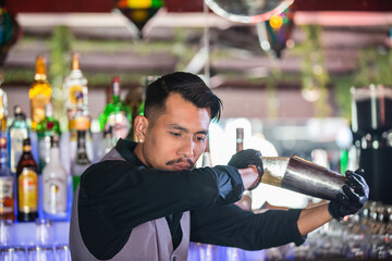 Expert asian bartender shaking cocktail at the bar using metal mixer over colorful background with...