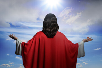 Jesus Christ with outstretched arms against blue sky, back view
