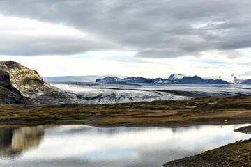 Glacier sloping down to the lake and mountainous terrain in the background. Cold majestic landscape. Iceland.

