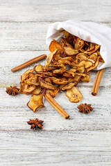 A pile of dried slices of pears and spices pills out of a white pouch on wooden background. Dried fruit chips.