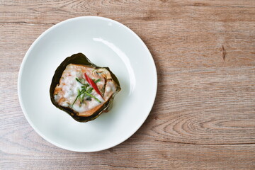steamed fish with curry paste in banana leaf tray on plate