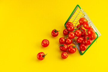 Scattered cherry tomatoes in a basket on a bright yellow background with an empty place for an inscription.