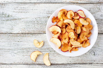 A pile of dried apples in slices on a white plate on wooden background. Dried fruit chips. Healthy food