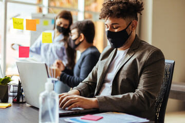 Business team wearing protective masks sitting at their desks separated by plexiglass dividers