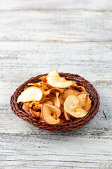 A pile of dried slices of apples in wicker basket on white wooden background. Dried fruit chips. Healthy food