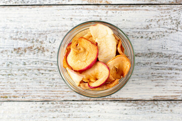 A pile of dried slices of apples in glass jar on white wooden background. Dried fruit chips. Healthy food
