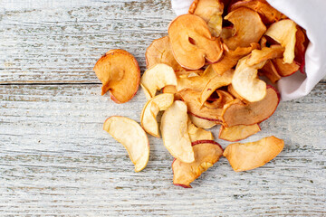 A pile of dried slices of apples pills out of a white pouch on wooden background. Dried fruit chips. Healthy food